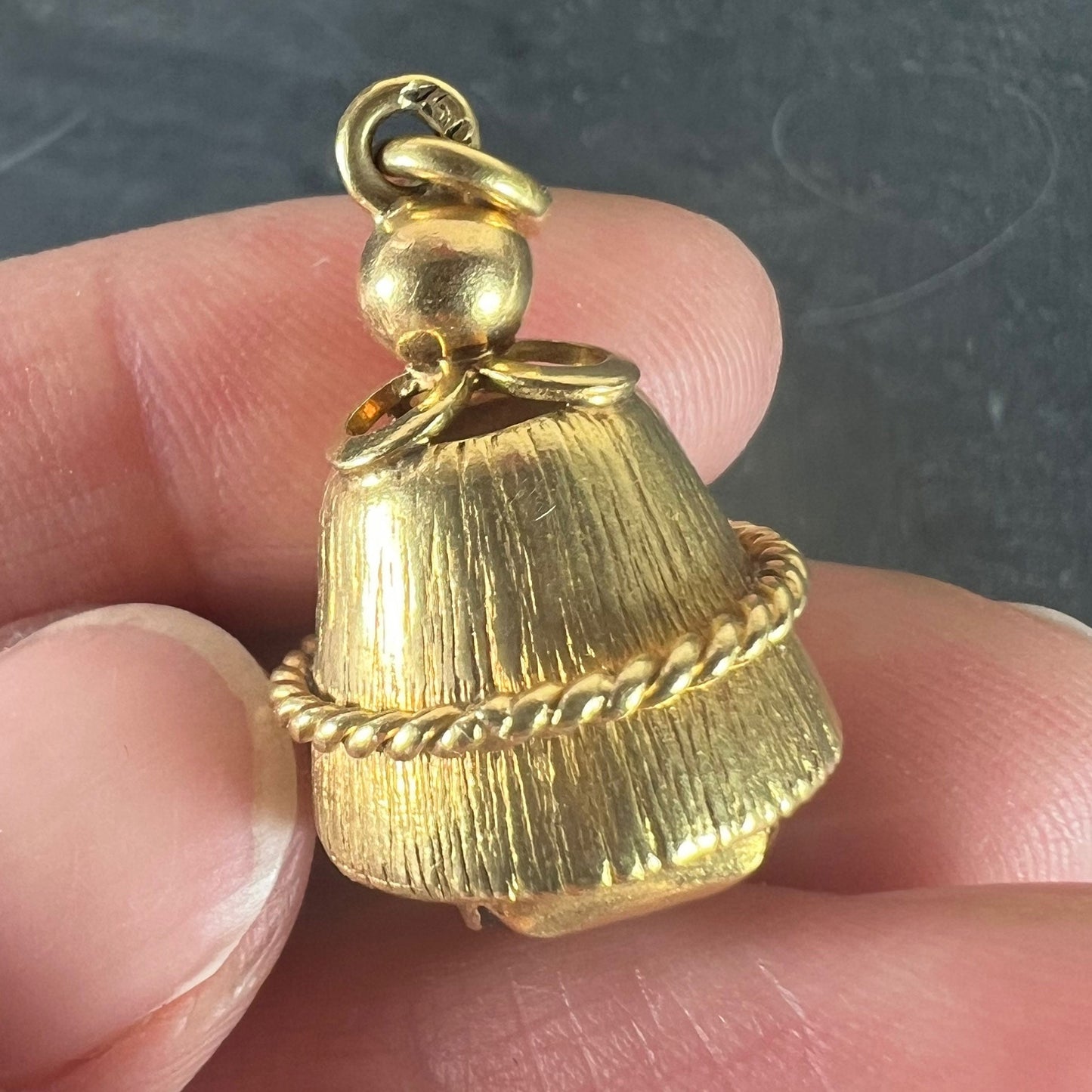 A yellow gold pendant held in a hand, on a grey background