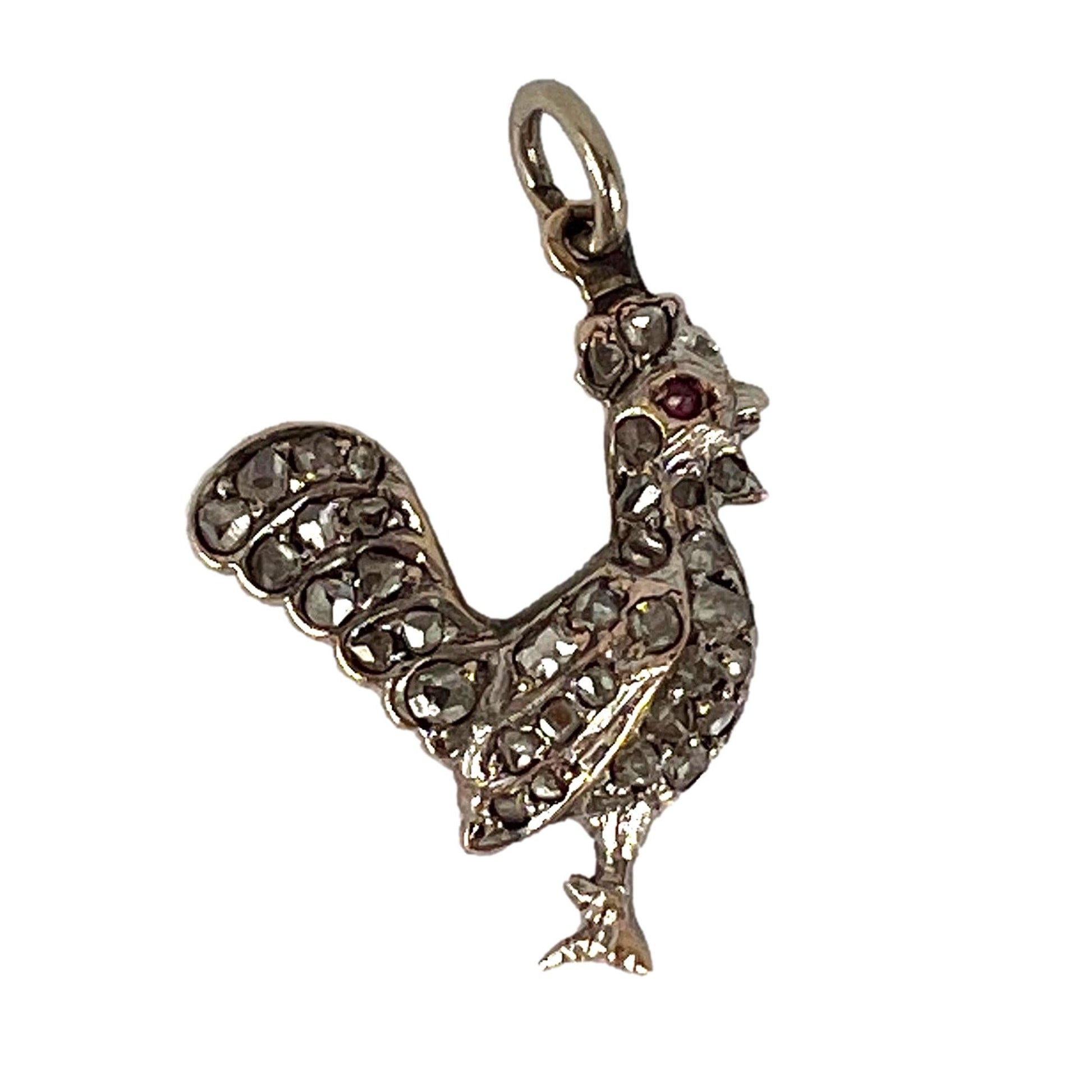 A rose cut diamond rooster pendant with a ruby eye, on a white background