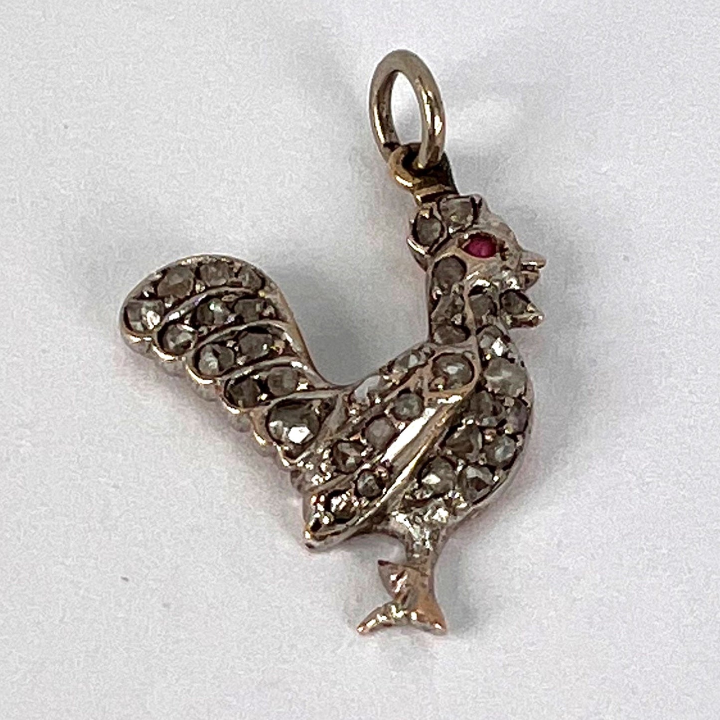 A rose cut diamond rooster pendant with a ruby eye, on a white background