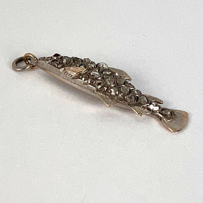 A fish shaped pendant with rose cut diamonds and ruby eye, on a white background