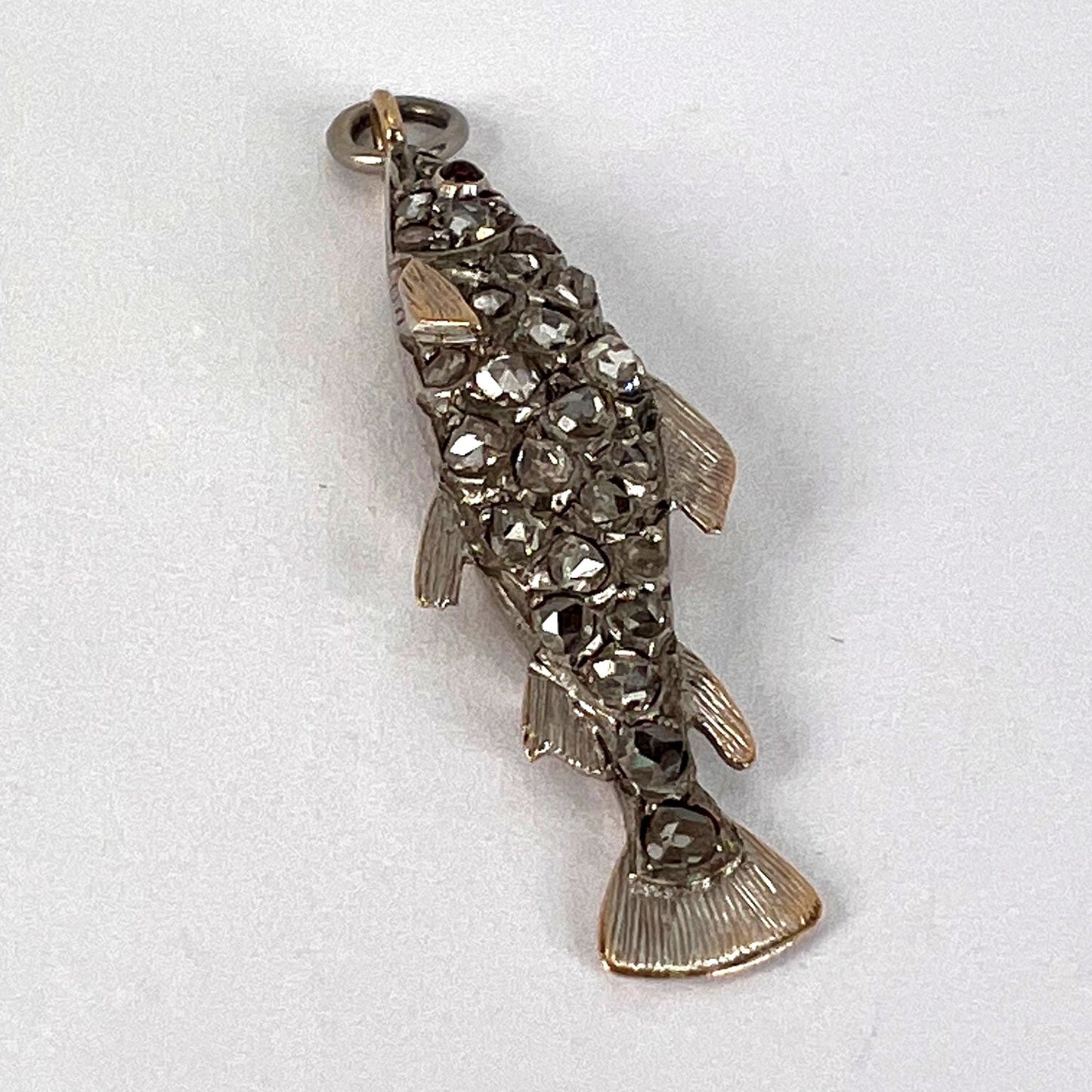 A fish shaped pendant with rose cut diamonds and ruby eye, on a white background