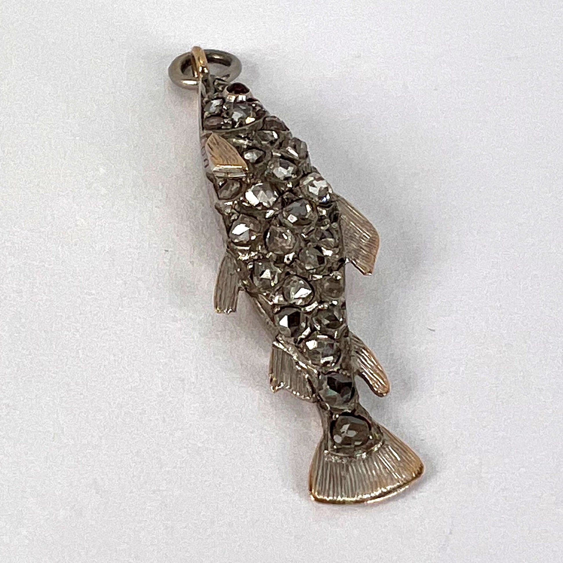 A fish shaped pendant with rose cut diamonds and ruby eye, on a white background