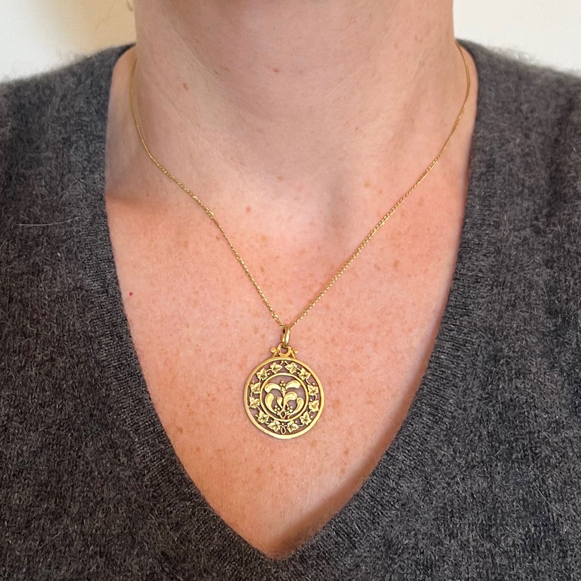 A round yellow gold pendant with mistletoe and ivy leaves, modelled on a gold chain