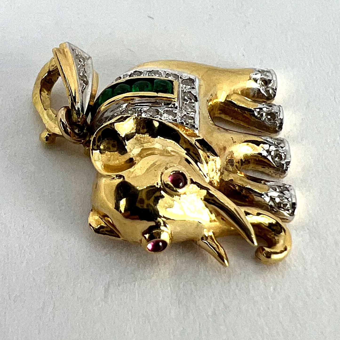 A yellow gold elephant pendant with rubies, emeralds and diamonds, on a white background