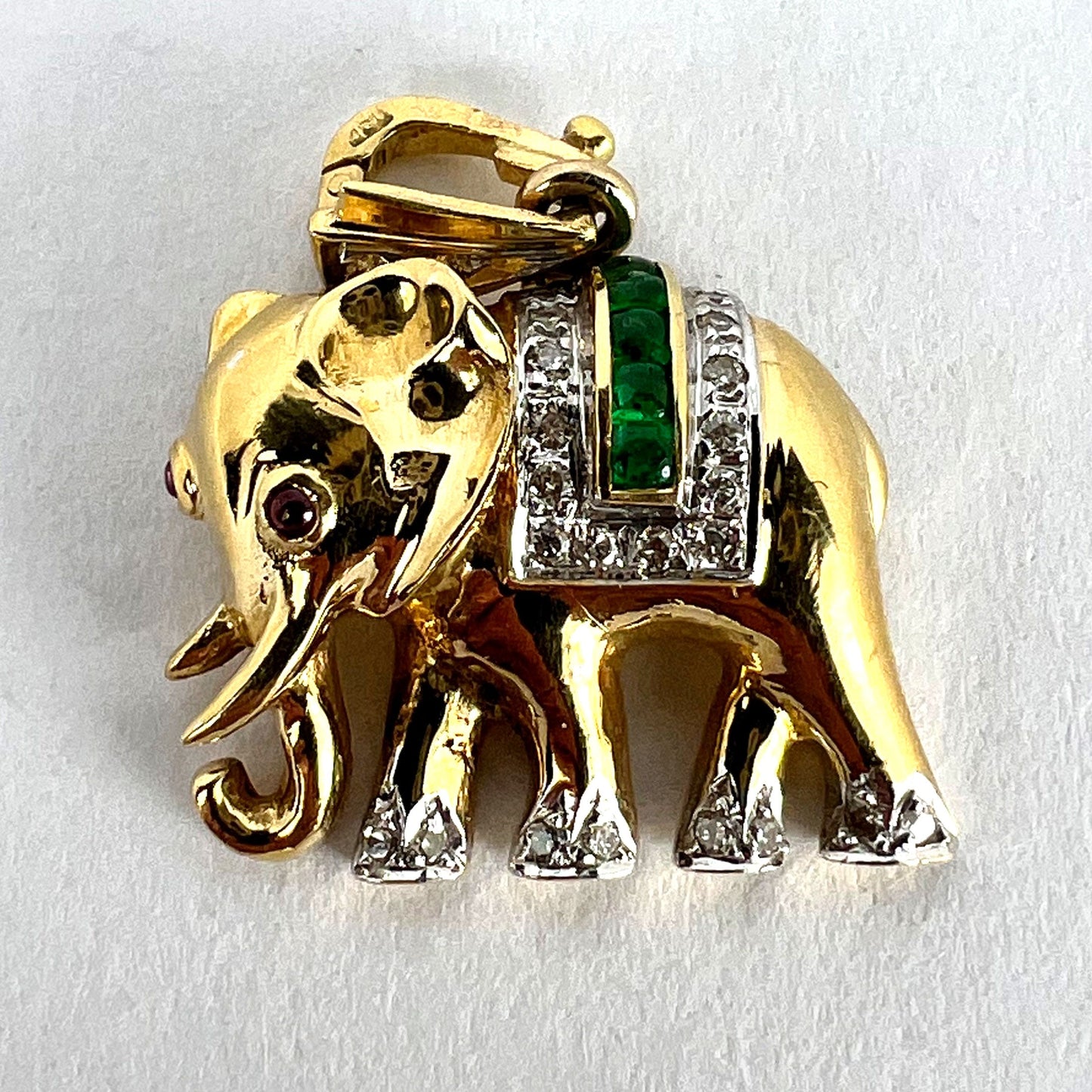 A yellow gold elephant pendant with rubies, emeralds and diamonds, on a white background
