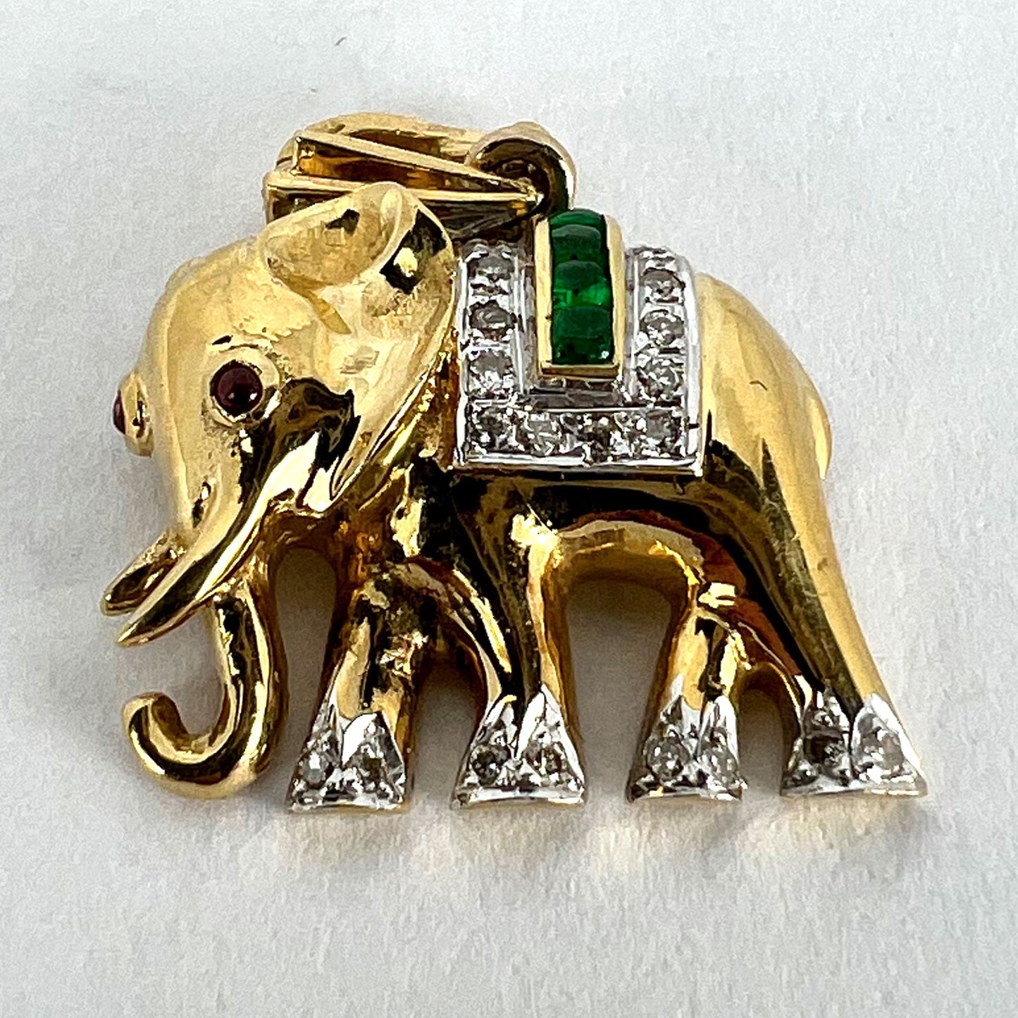 A yellow gold elephant pendant with rubies, emeralds and diamonds, on a white background