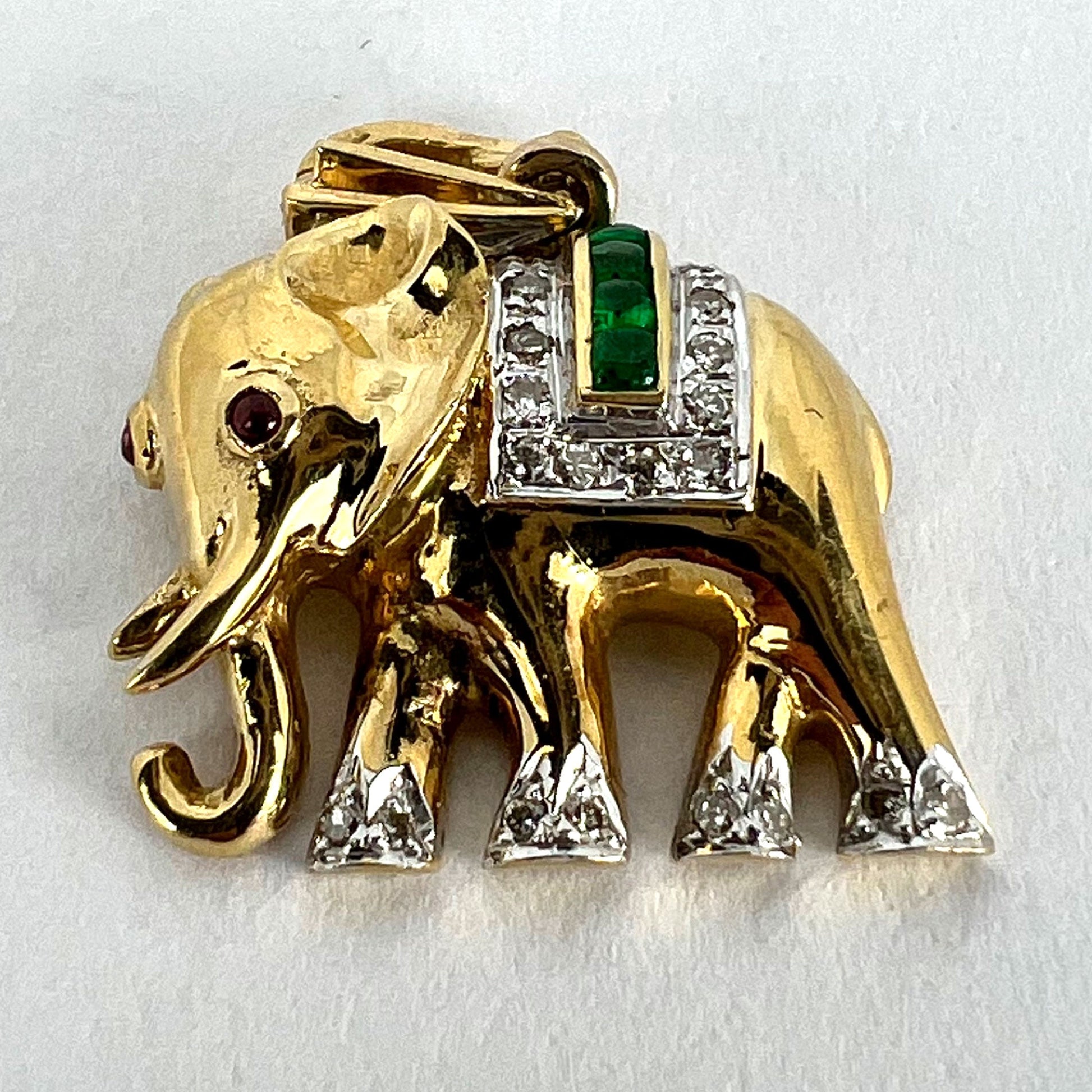 A yellow gold elephant pendant with rubies, emeralds and diamonds, on a white background
