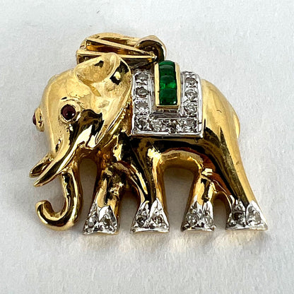A yellow gold elephant pendant with rubies, emeralds and diamonds, on a white background