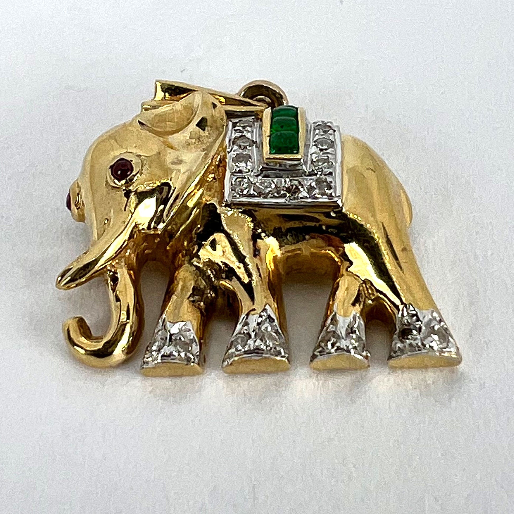 A yellow gold elephant pendant with rubies, emeralds and diamonds, on a white background