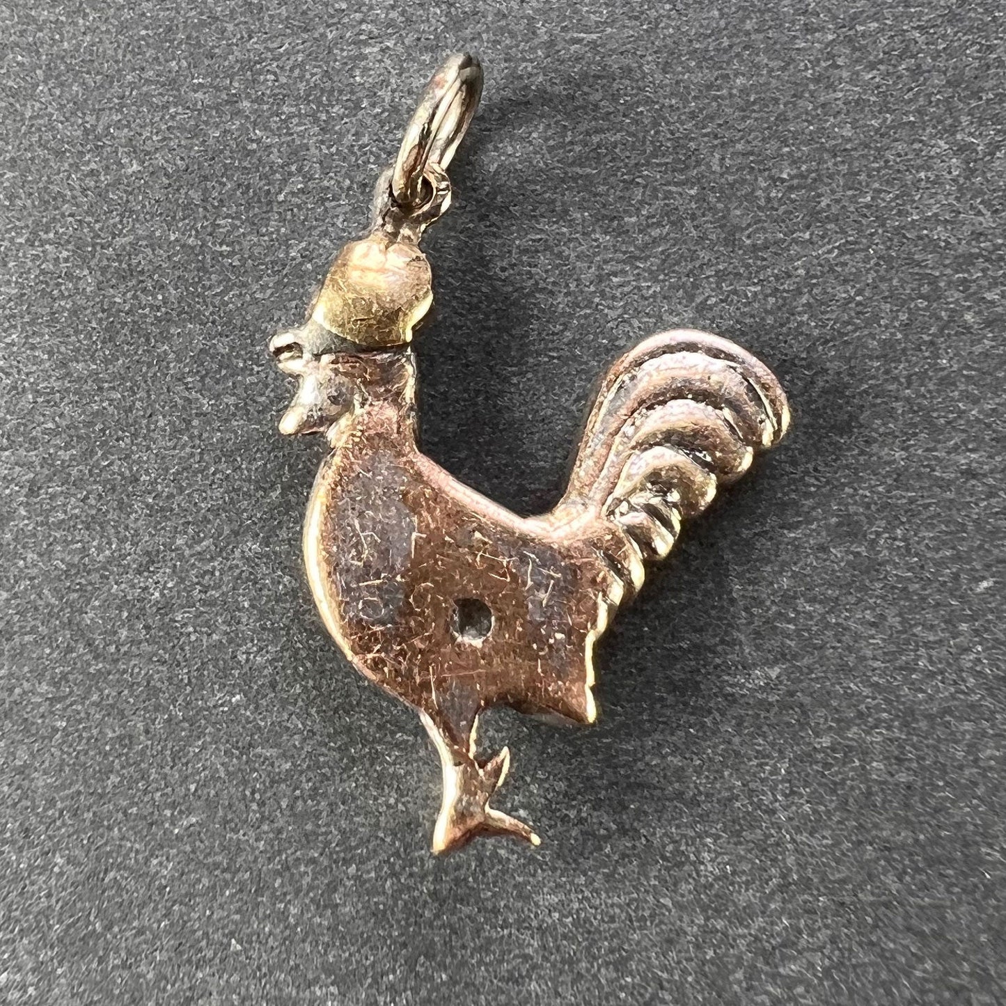 A gold rooster pendant, on a grey background