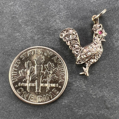 A rose cut diamond rooster pendant with a ruby eye, next to a dime coin on a grey background