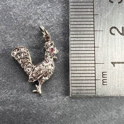 A rose cut diamond rooster pendant with a ruby eye, next to a metal ruler on a grey background