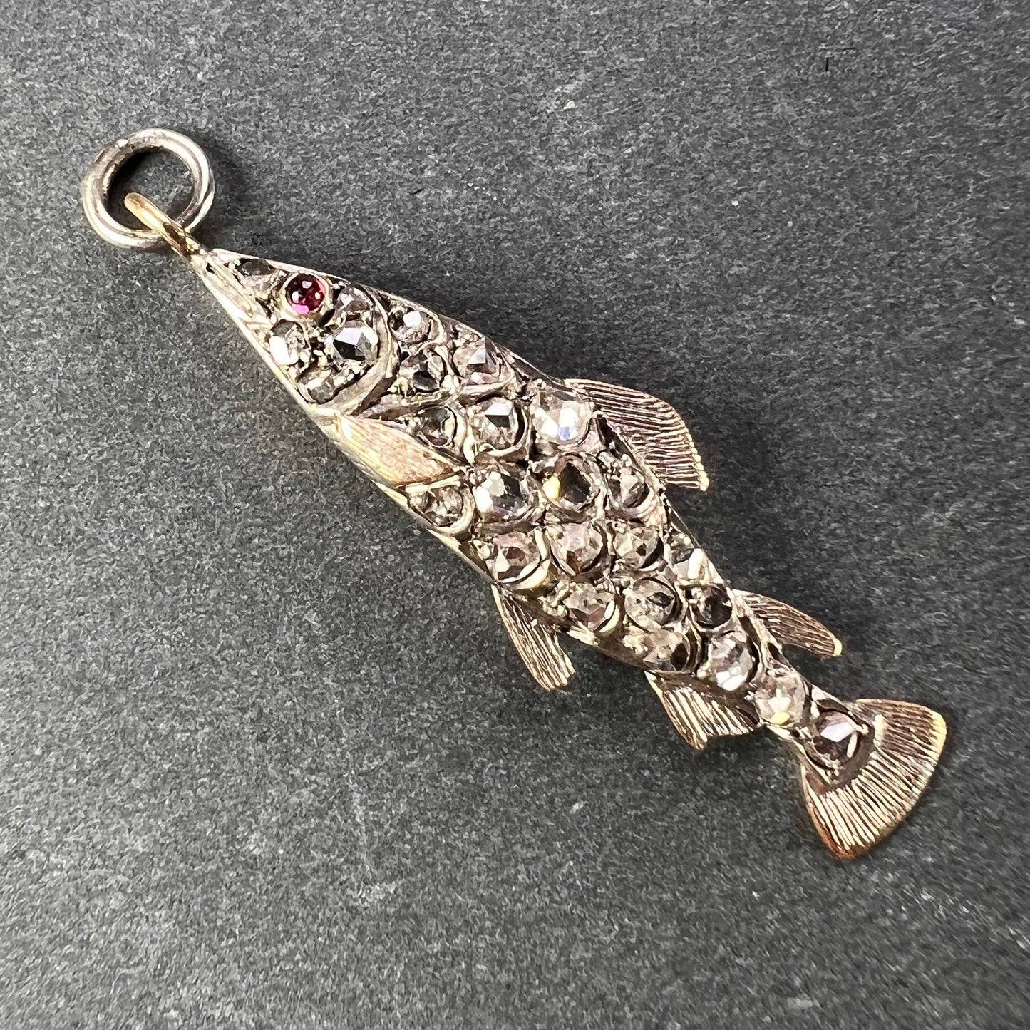 A fish shaped pendant with rose cut diamonds and ruby eye, on a grey background