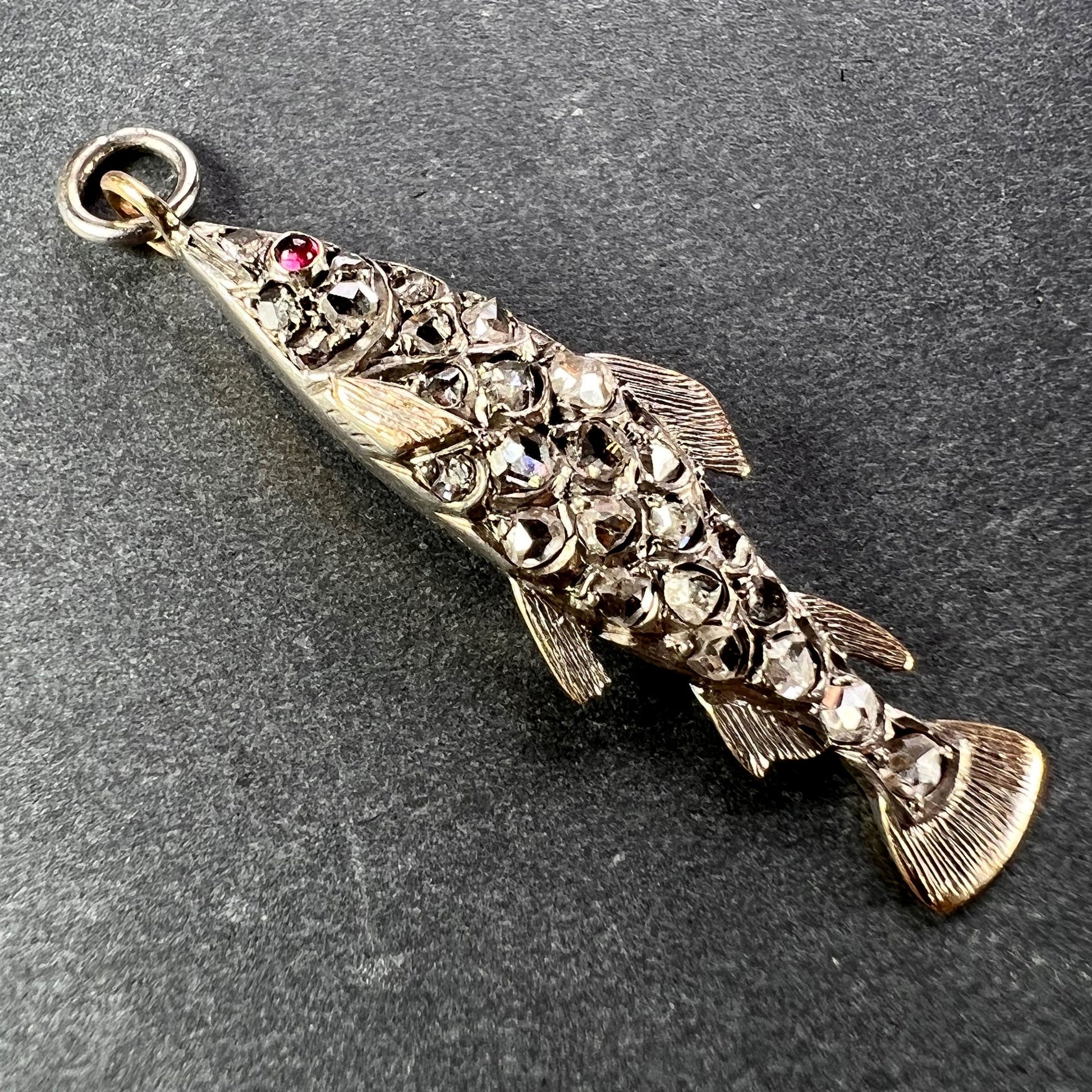 A fish shaped pendant with rose cut diamonds and ruby eye, on a grey background