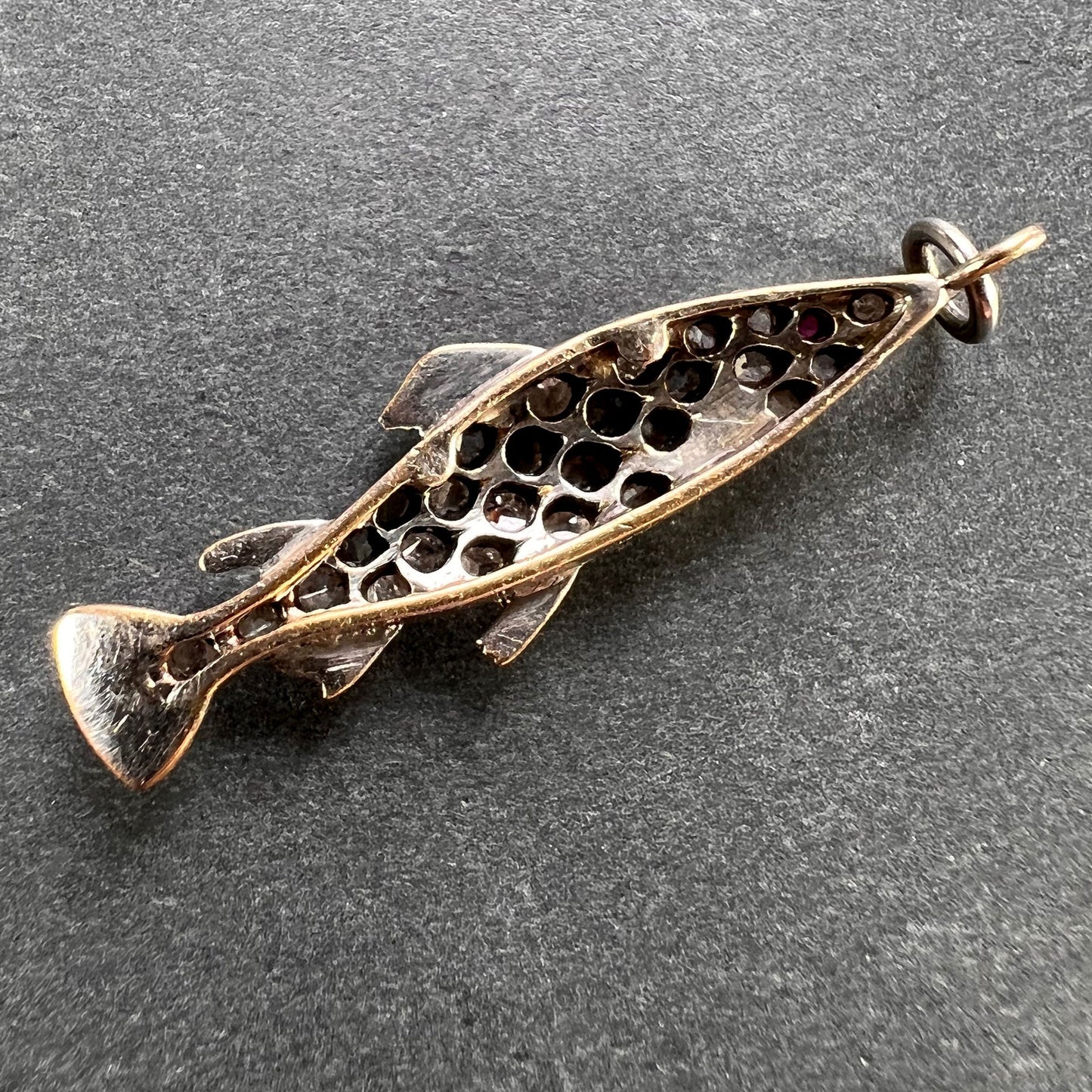 A fish shaped pendant with rose cut diamonds and ruby eye, on a grey background