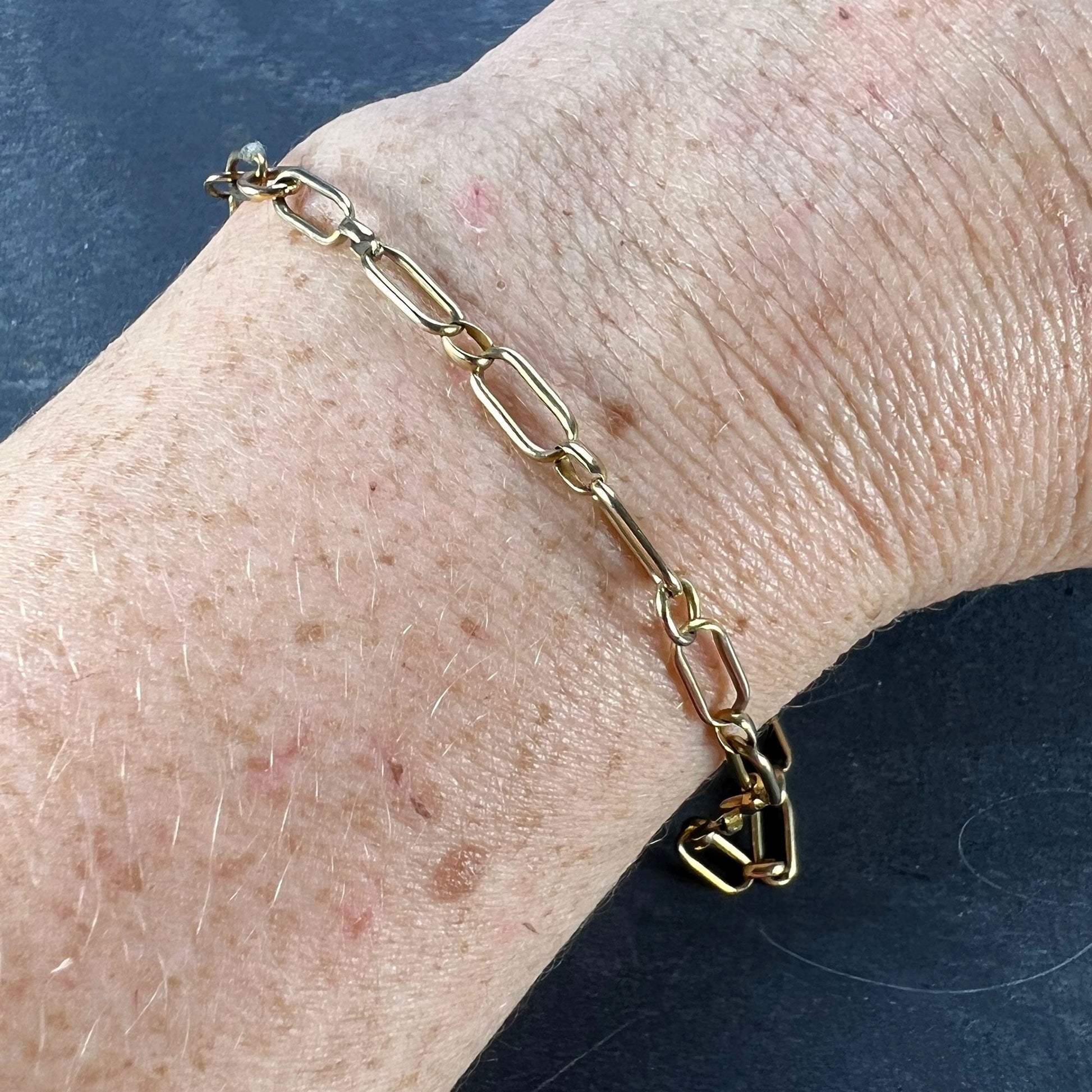 A yellow gold link bracelet with bolt ring clasp, modelled on a wrist on a grey background