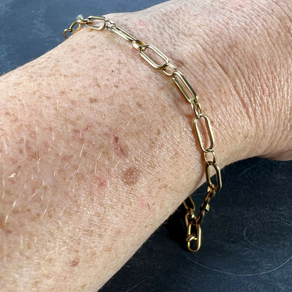 A yellow gold link bracelet with bolt ring clasp, modelled on a wrist on a grey background