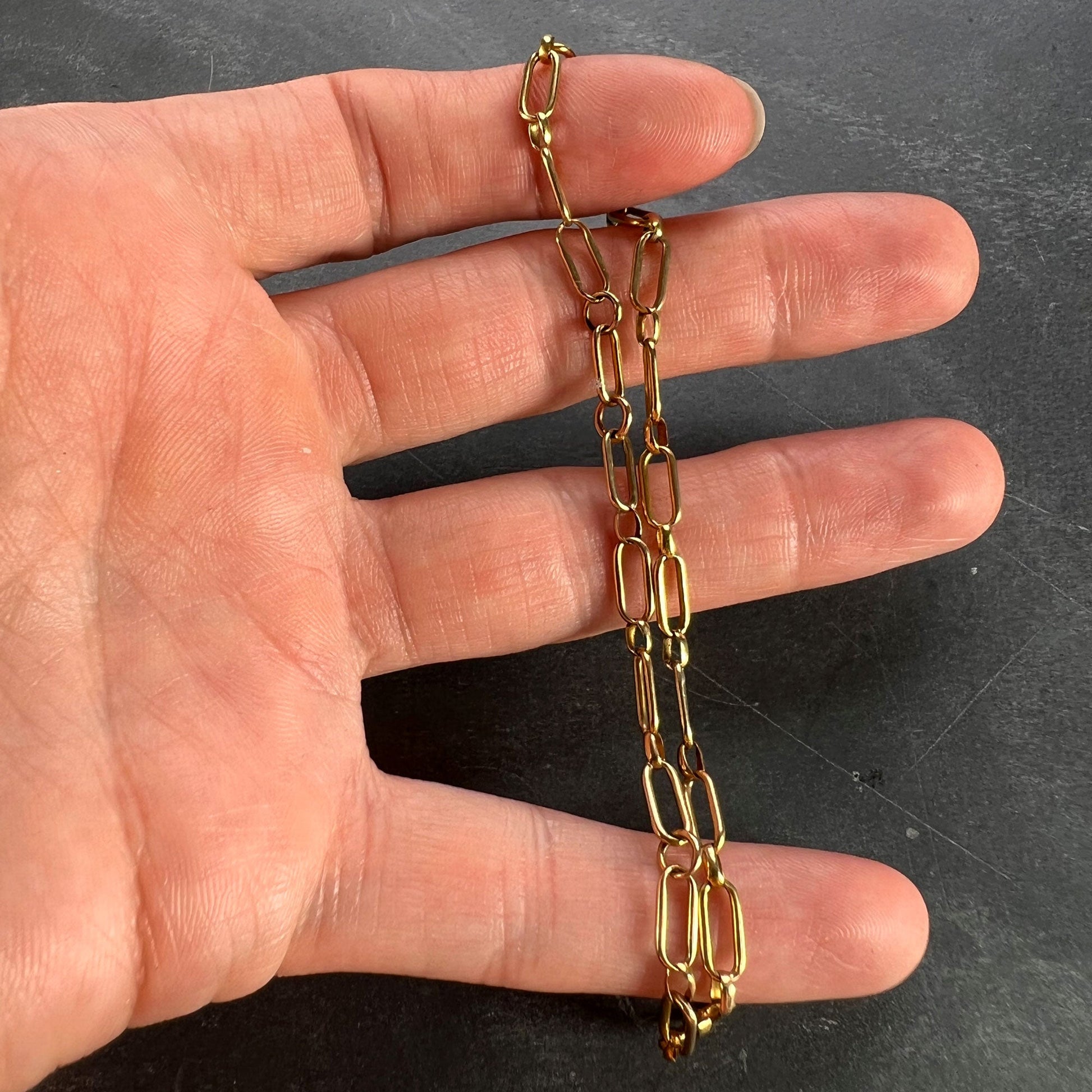 A yellow gold link bracelet with bolt ring clasp, held in a hand on a grey background