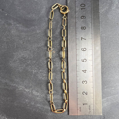 A yellow gold link bracelet with bolt ring clasp, next to a metal ruler on a grey background