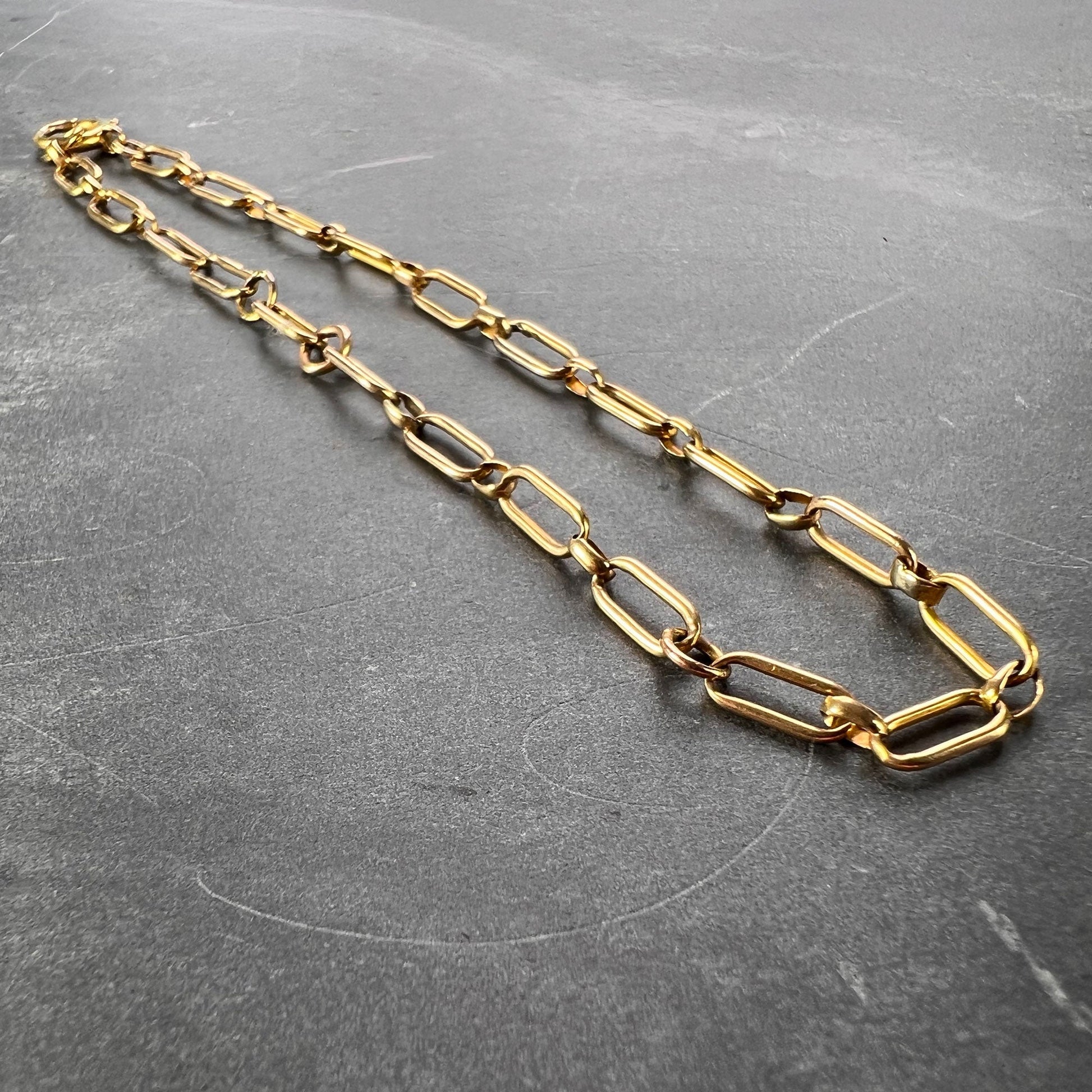 A yellow gold link bracelet with bolt ring clasp, on a grey background