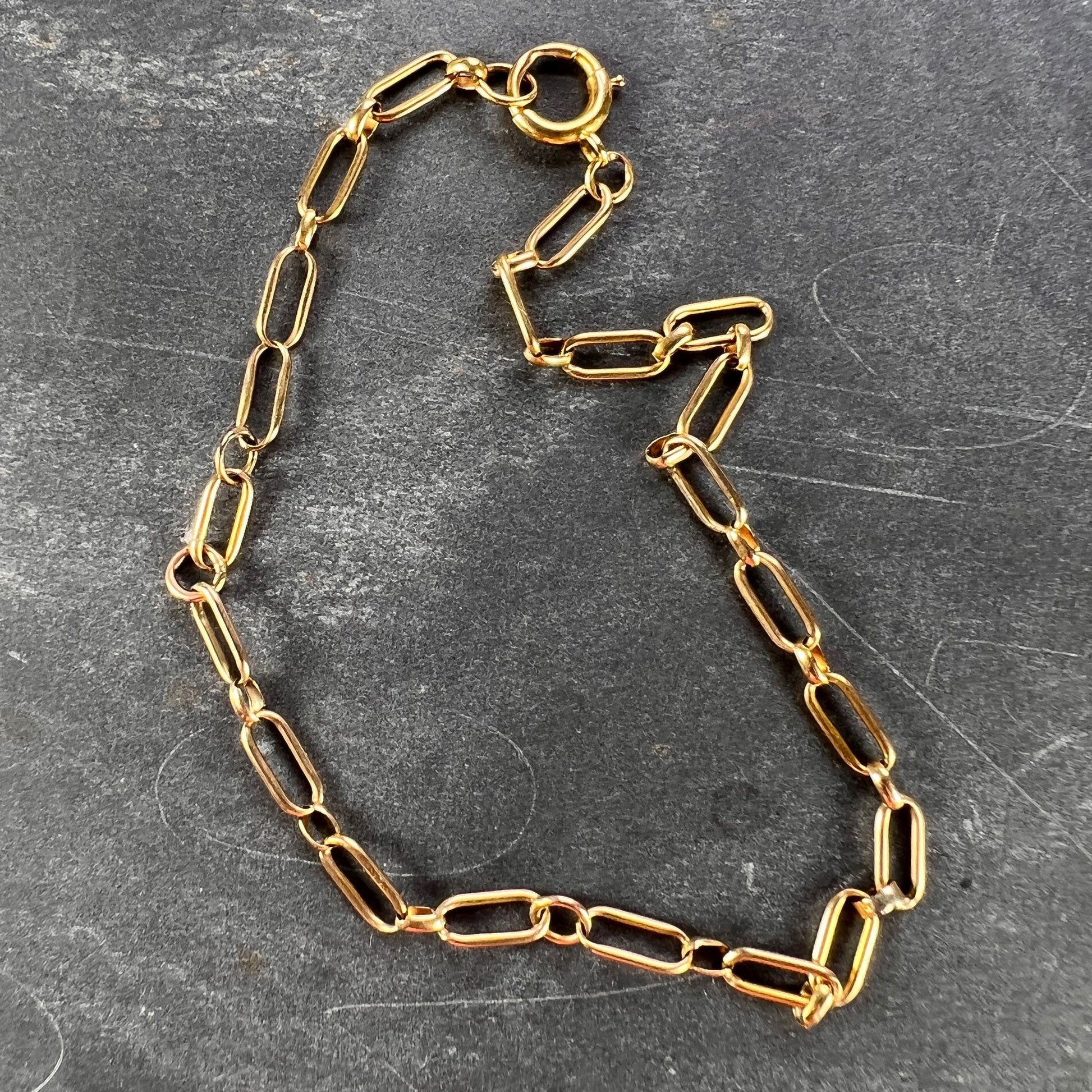 A yellow gold link bracelet with bolt ring clasp, on a grey background