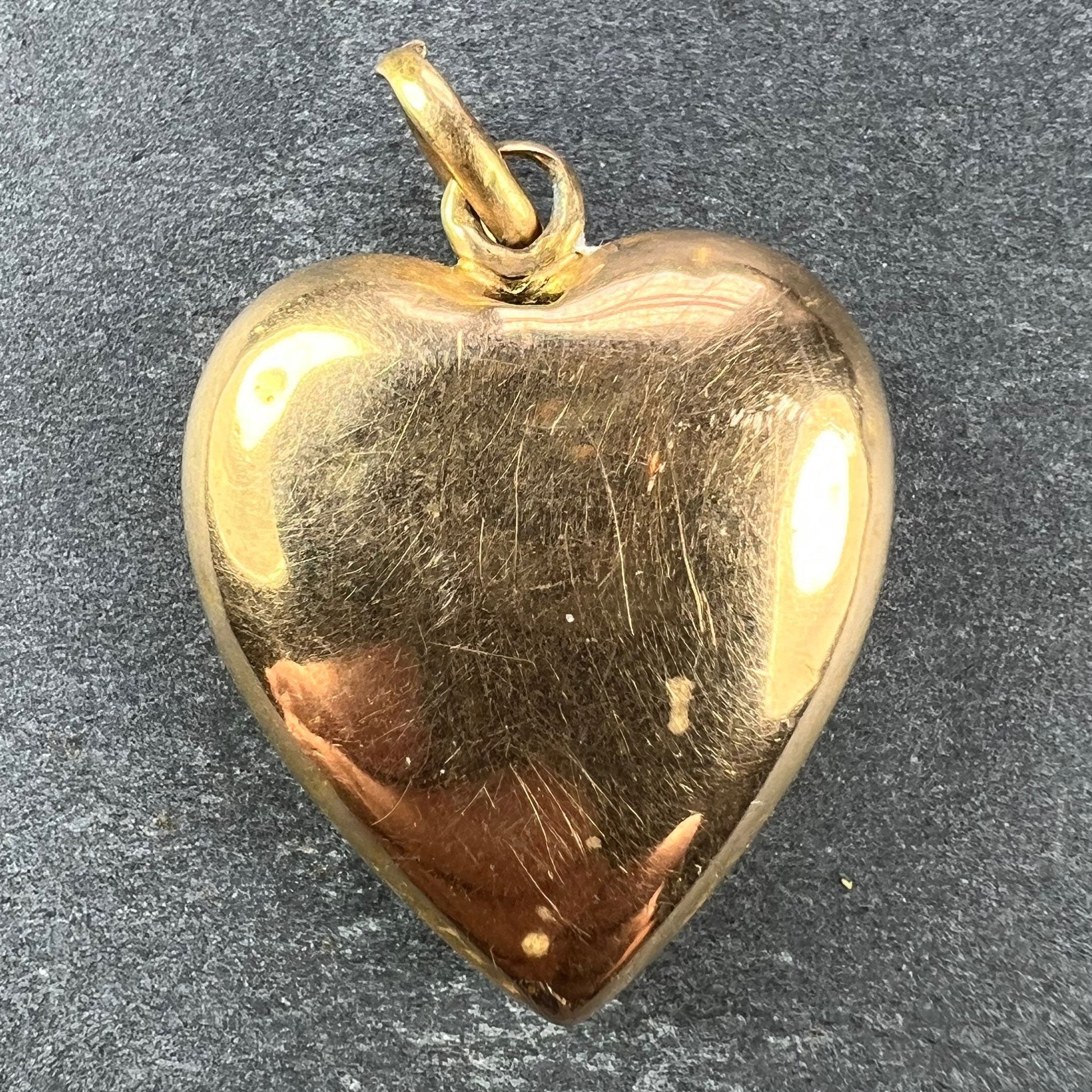 A yellow gold heart shaped pendant, on a grey background