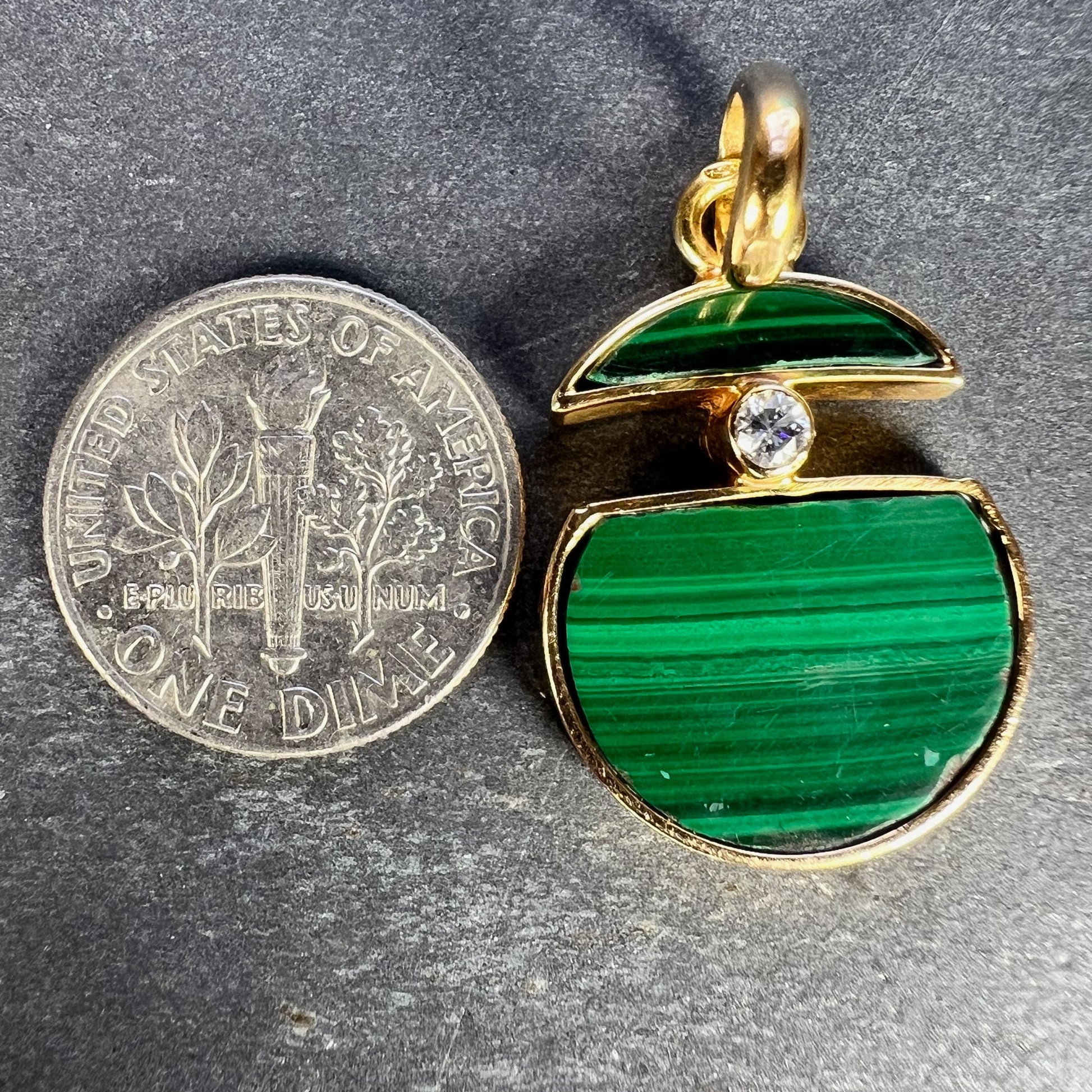A malachite and diamond yellow gold split circle pendant, next to a dime coin on a grey background