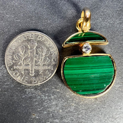A malachite and diamond yellow gold split circle pendant, next to a dime coin on a grey background