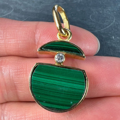 A malachite and diamond yellow gold split circle pendant, held in a hand on a grey background
