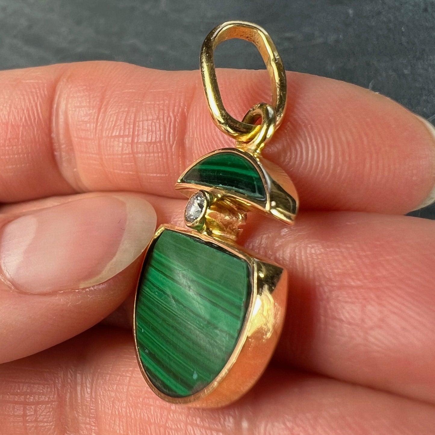 A malachite and diamond yellow gold split circle pendant, held in a hand on a grey background