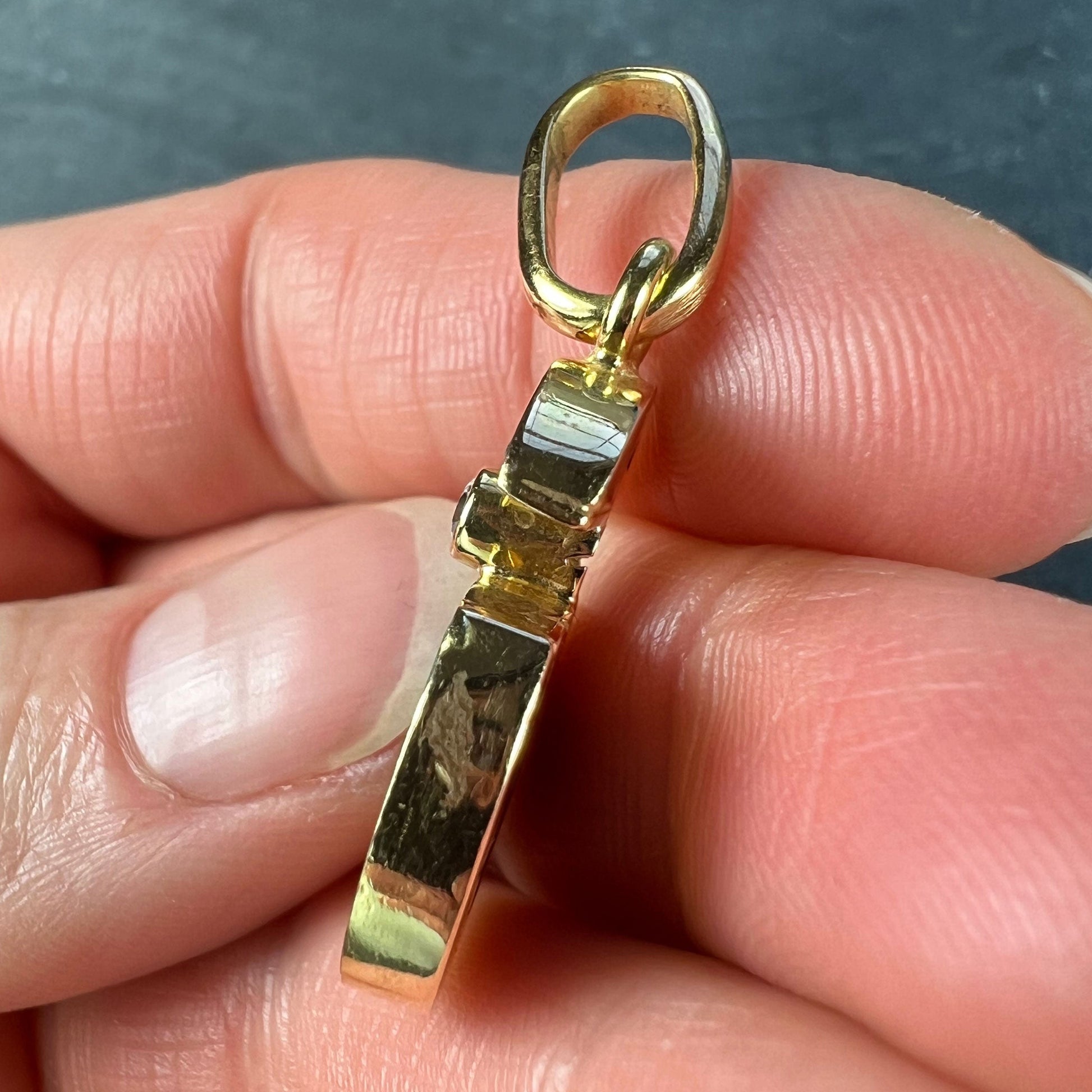 A malachite and diamond yellow gold split circle pendant, held in a hand on a grey background