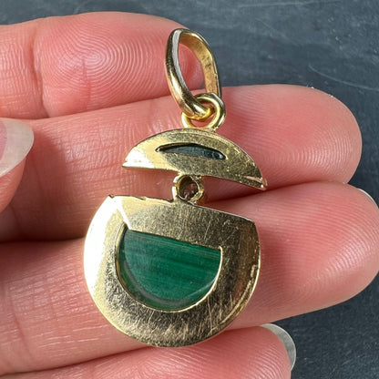 A malachite and diamond yellow gold split circle pendant, held in a hand on a grey background