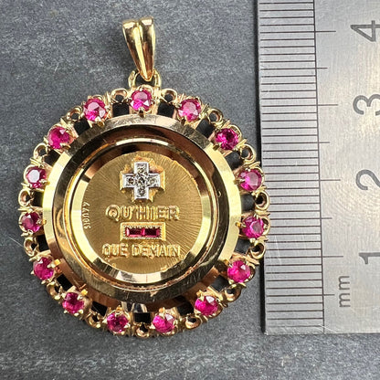 A French QU'HIER QUE DEMAIN pendant with diamonds and synthetic rubies, next to a metal ruler on a grey background