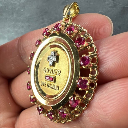 A French QU'HIER QUE DEMAIN pendant with diamonds and synthetic rubies, held in a hand on a grey background