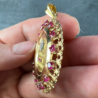 A French QU'HIER QUE DEMAIN pendant with diamonds and synthetic rubies, held in a hand on a grey background