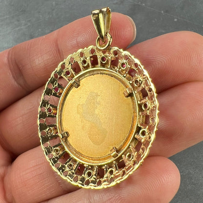 A round yellow gold pendant, held in a hand on a grey background