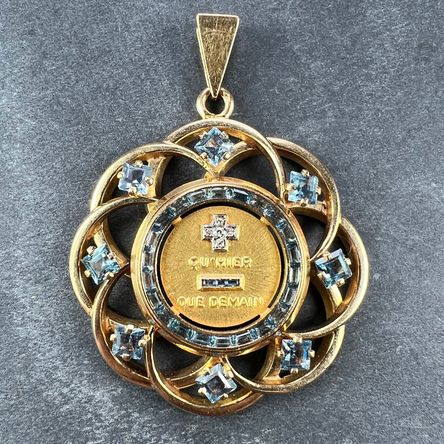 A yellow gold French QU'HIER QUE DEMAIN pendant with blue stones and diamonds, on a grey background