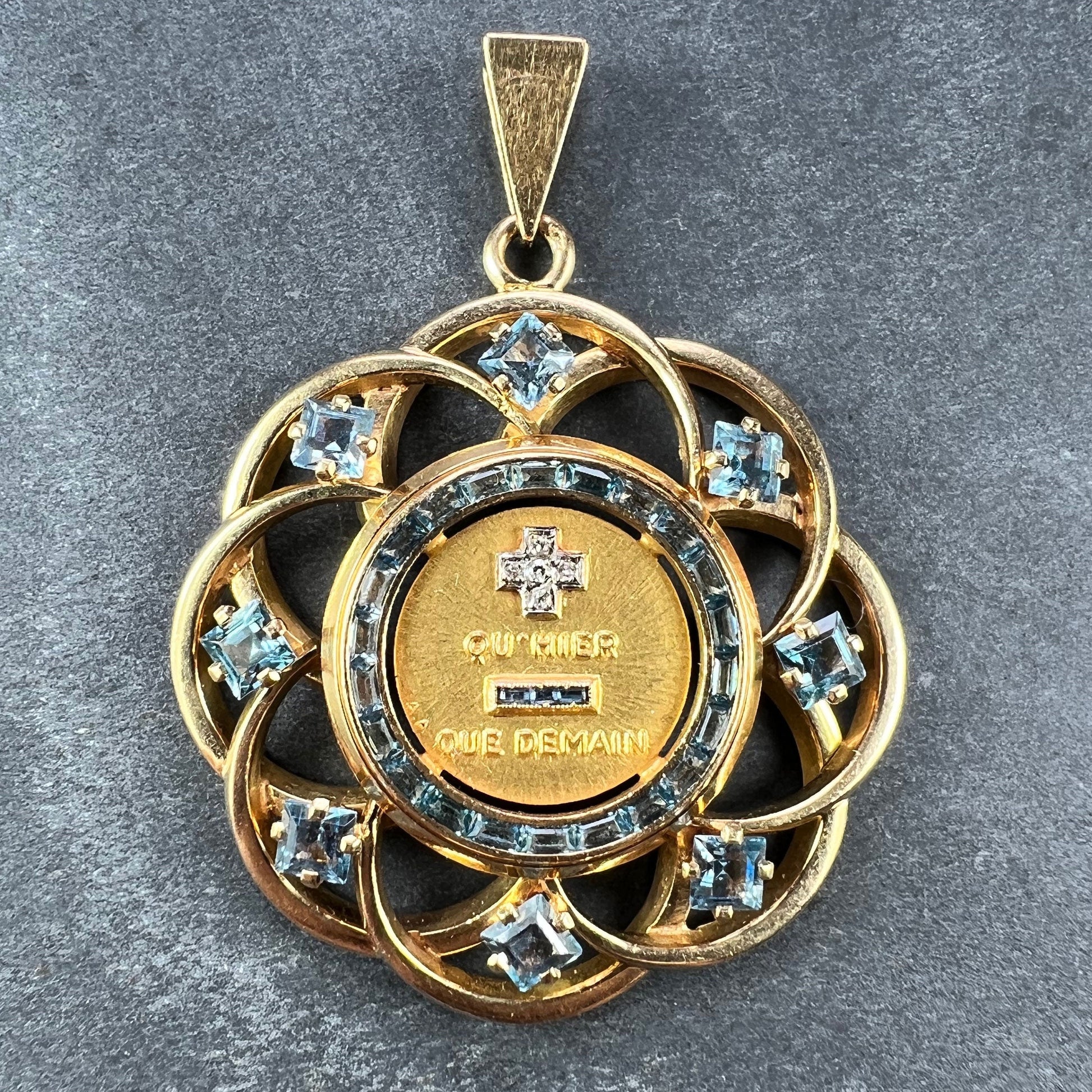 A yellow gold French QU'HIER QUE DEMAIN pendant with blue stones and diamonds, on a grey background