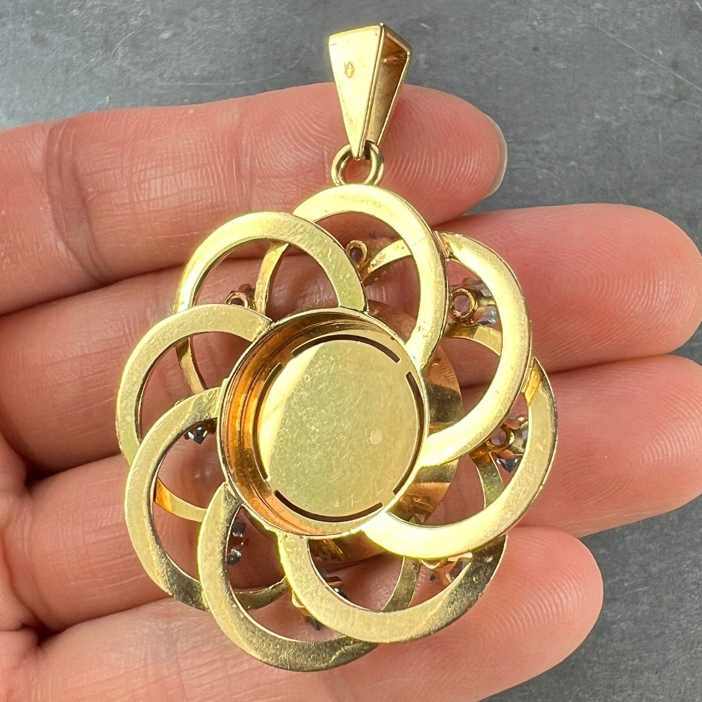 A yellow gold pendant, held in a hand on a grey background
