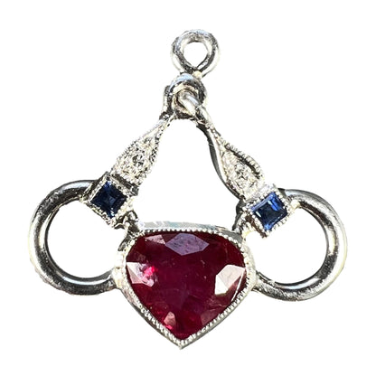 A heart shaped pendant with snaffle bits in white metal, with red, white and blue gemstones, on a white background
