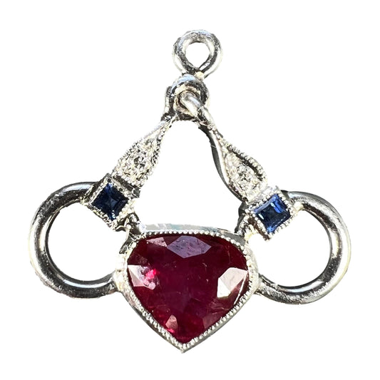 A heart shaped pendant with snaffle bits in white metal, with red, white and blue gemstones, on a white background