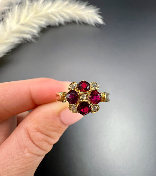 A ruby and diamond cross design ring in yellow gold, held in a hand
