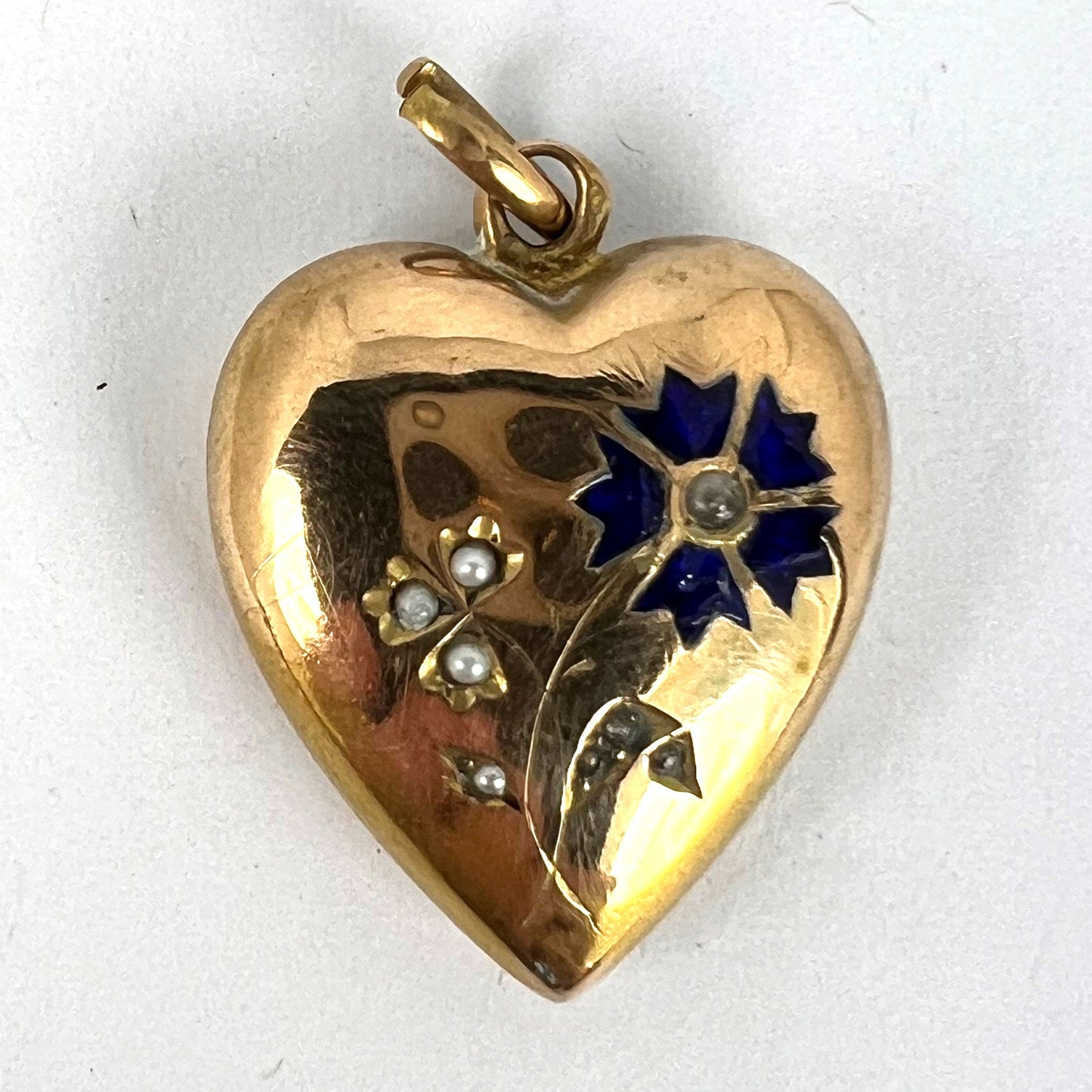 A yellow gold heart shaped pendant with enamel and seed pearls, on a white background