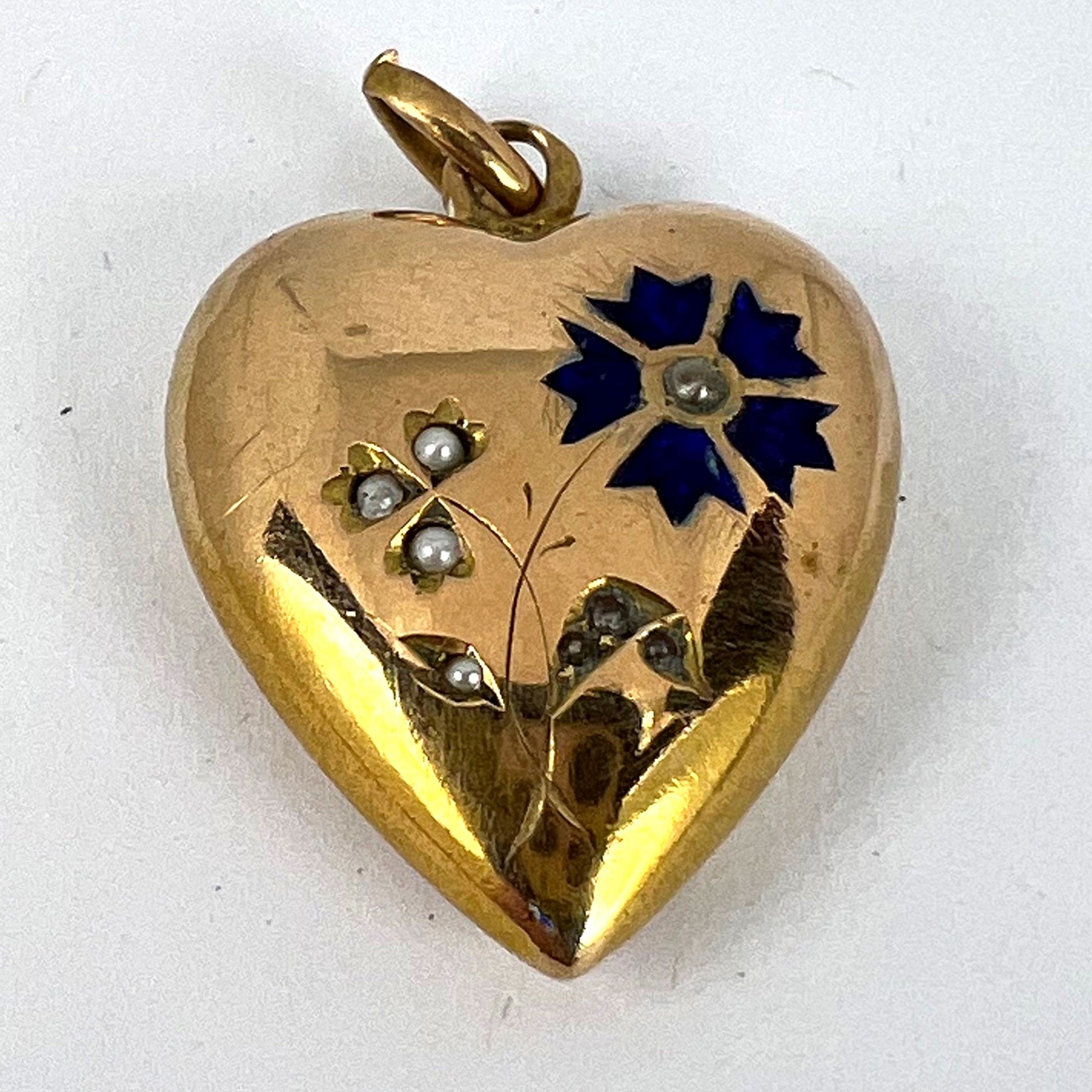 A yellow gold heart shaped pendant with enamel and seed pearls, on a white background