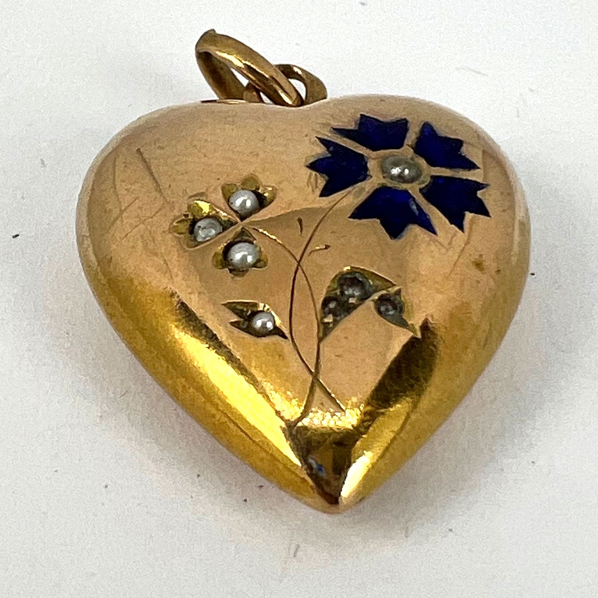 A yellow gold heart shaped pendant with enamel and seed pearls, on a white background