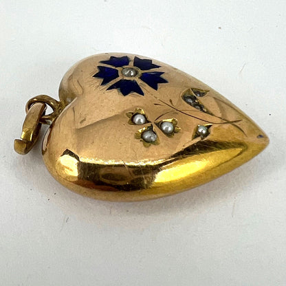 A yellow gold heart shaped pendant with enamel and seed pearls, on a white background