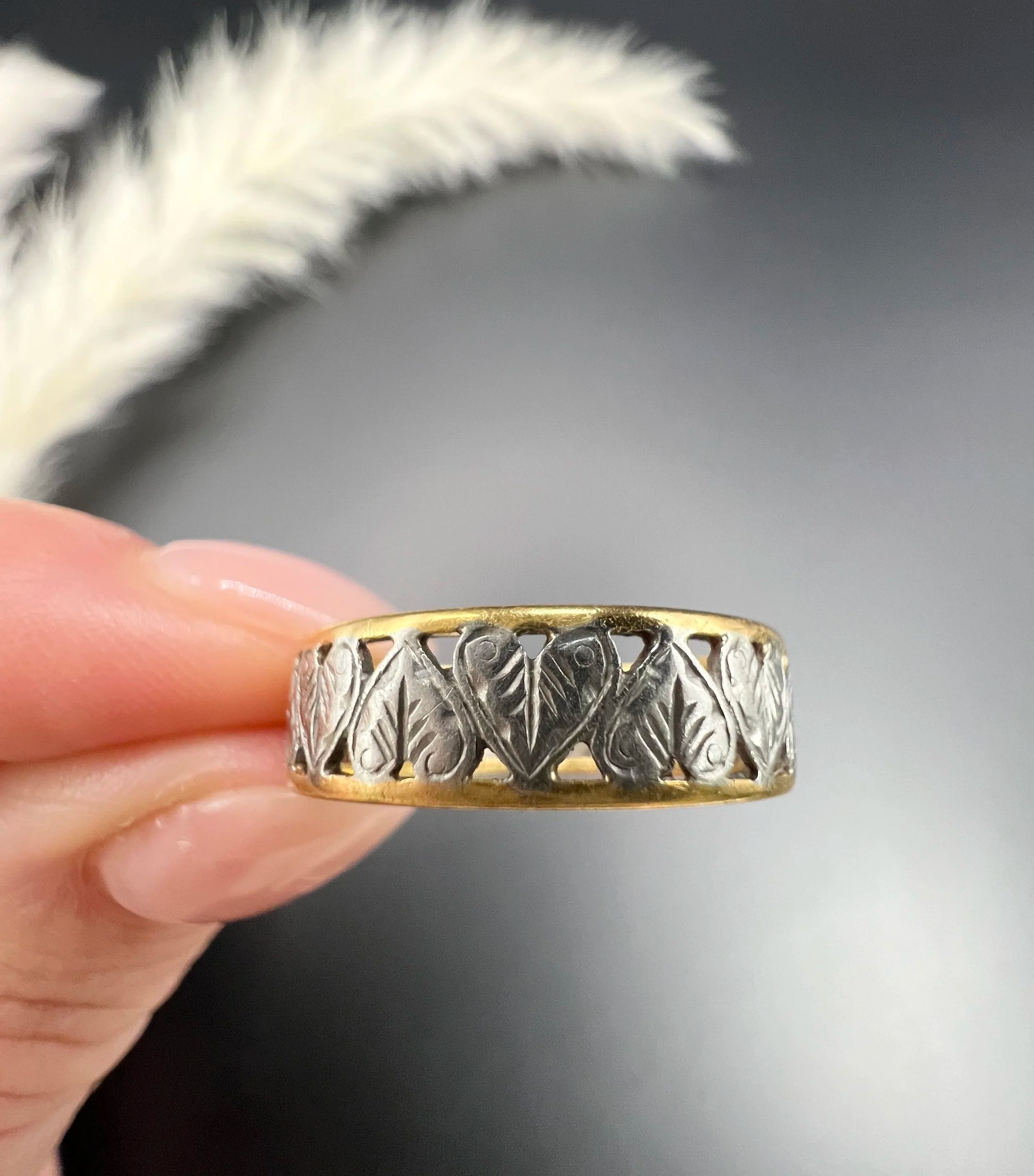 A yellow gold and platinum heart cutout band ring, held in a hand