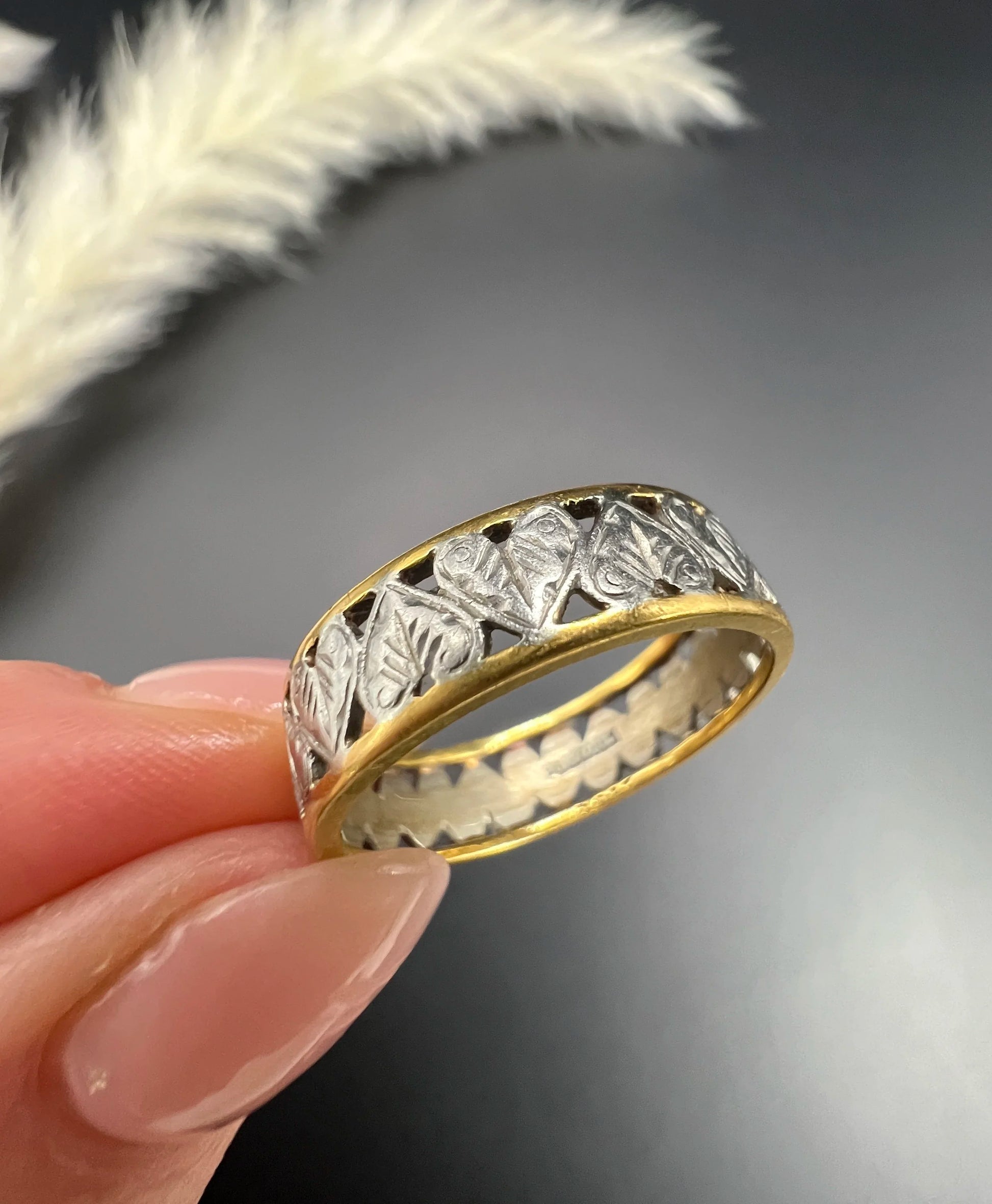 A yellow gold and platinum heart cutout band ring, held in a hand