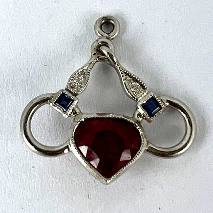 A heart shaped pendant with snaffle bits in white metal, with red, white and blue gemstones, on a white background