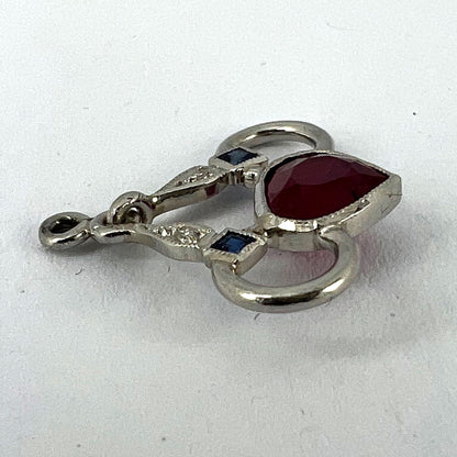 A heart shaped pendant with snaffle bits in white metal, with red, white and blue gemstones, on a white background